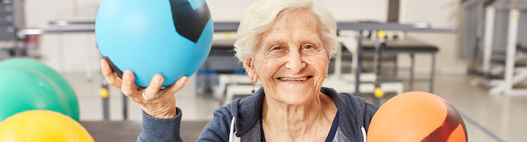 Senior woman poses with medicine balls in workout area.